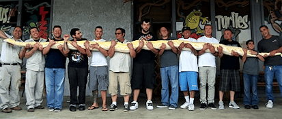 Group of people holding a large albino python outside a reptile store, showcasing the snake's length and size in a community setting.